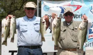Two men holding up their fish in front of a banner.