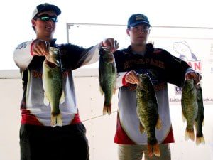 Two men are holding up their fish on a boat.