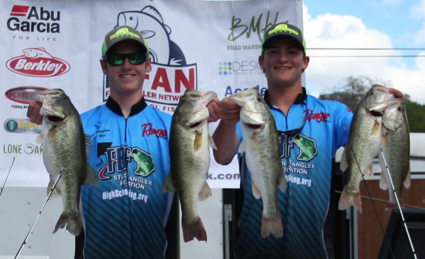 Two young men holding up their fish at a tournament.