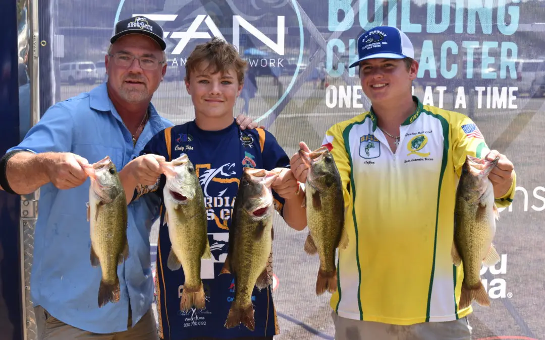 Three men are holding up their fish at a tournament.