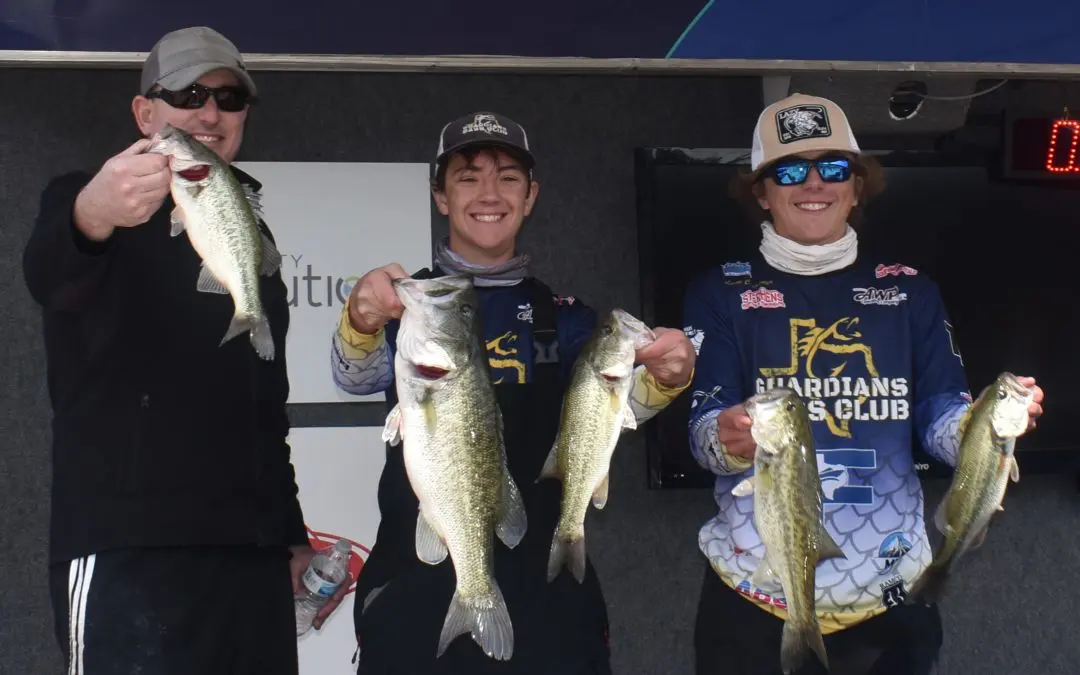 Three men are holding up their bass on a boat.