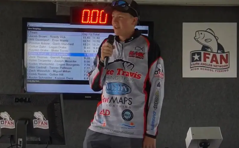 A man is speaking into a microphone in front of a large screen.