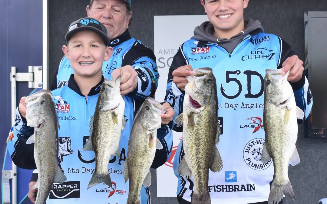 Three young men holding up their fish at a tournament.