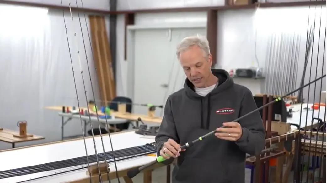 A man is holding a fishing rod in a workshop.