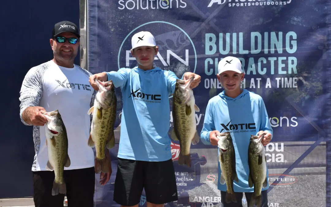 Three people holding up fish in front of a sign.