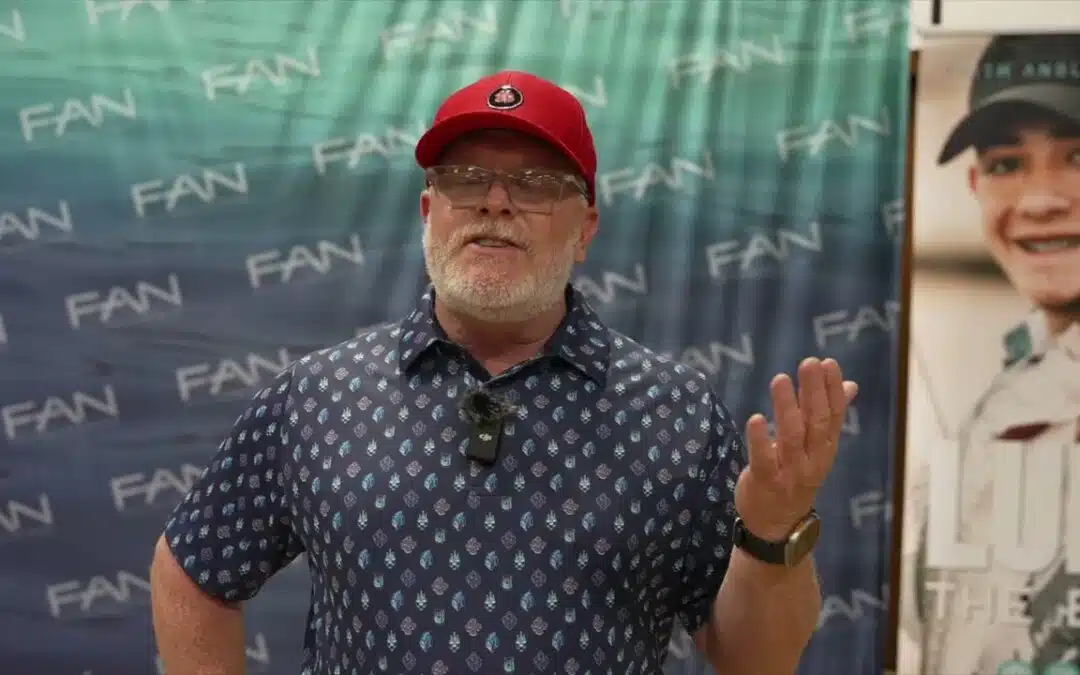 Man in red cap speaking at event.