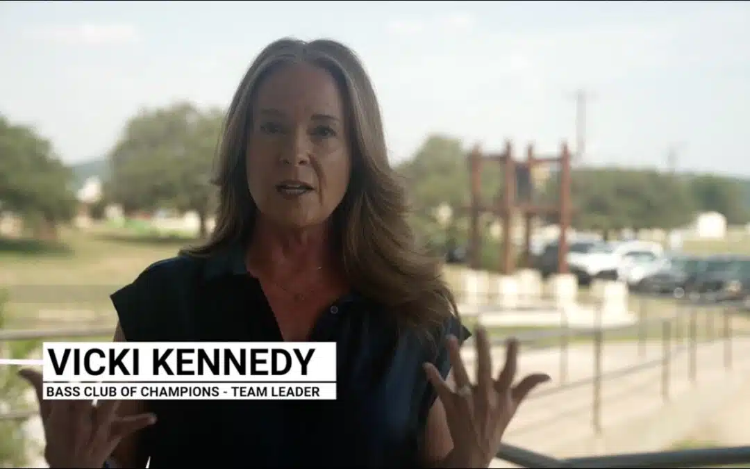 Woman speaking outdoors, trees in background.